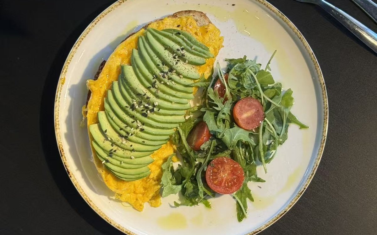 Avocado toast di FYSA visto dall'alto: sourdough tostato, uova strapazzate, avocado a ventaglio e sesamo, con rucola e pomodorini