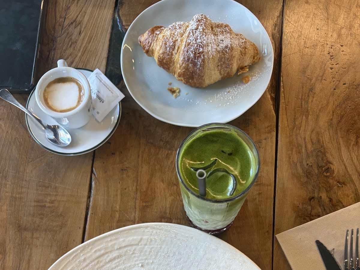Cappuccino, croissant e matcha su tavolo in legno
