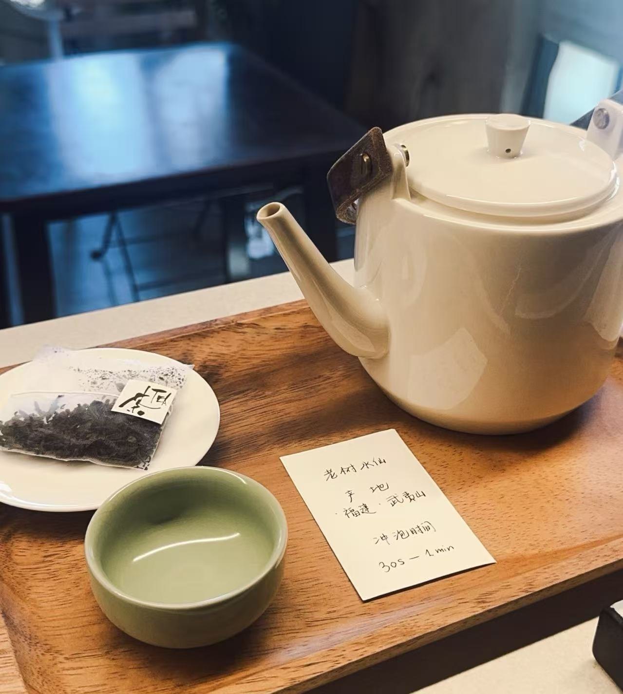 Chinese tea served at FYSA: a white teapot on a wooden tray, a pale green cup and a handwritten card with the tea's name, origin and steeping time